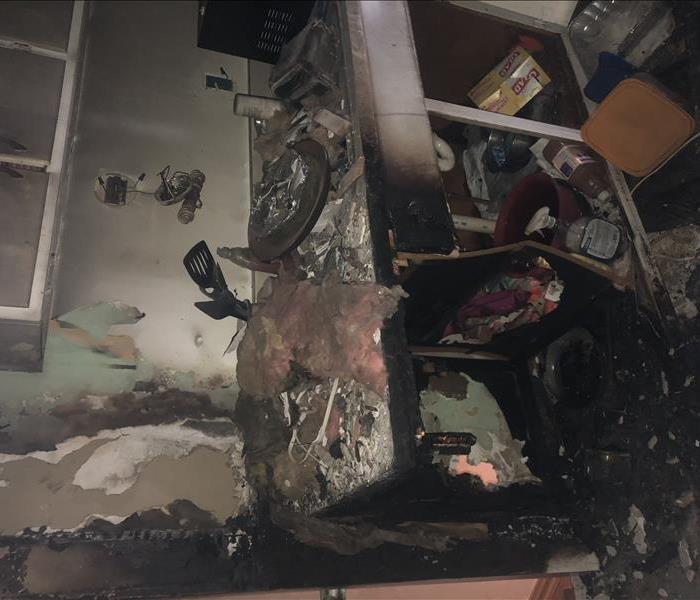 A kitchen with severe fire damaged.  Holes in the drywall, charred debris, soot stained walls.
